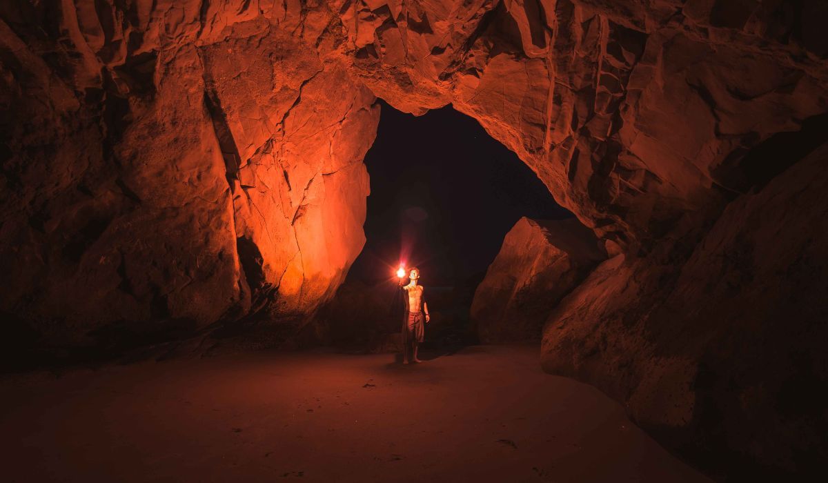 Silhouette di uomo che giunge al termine di un sentiero tra alberi e illuminato da luce intensa